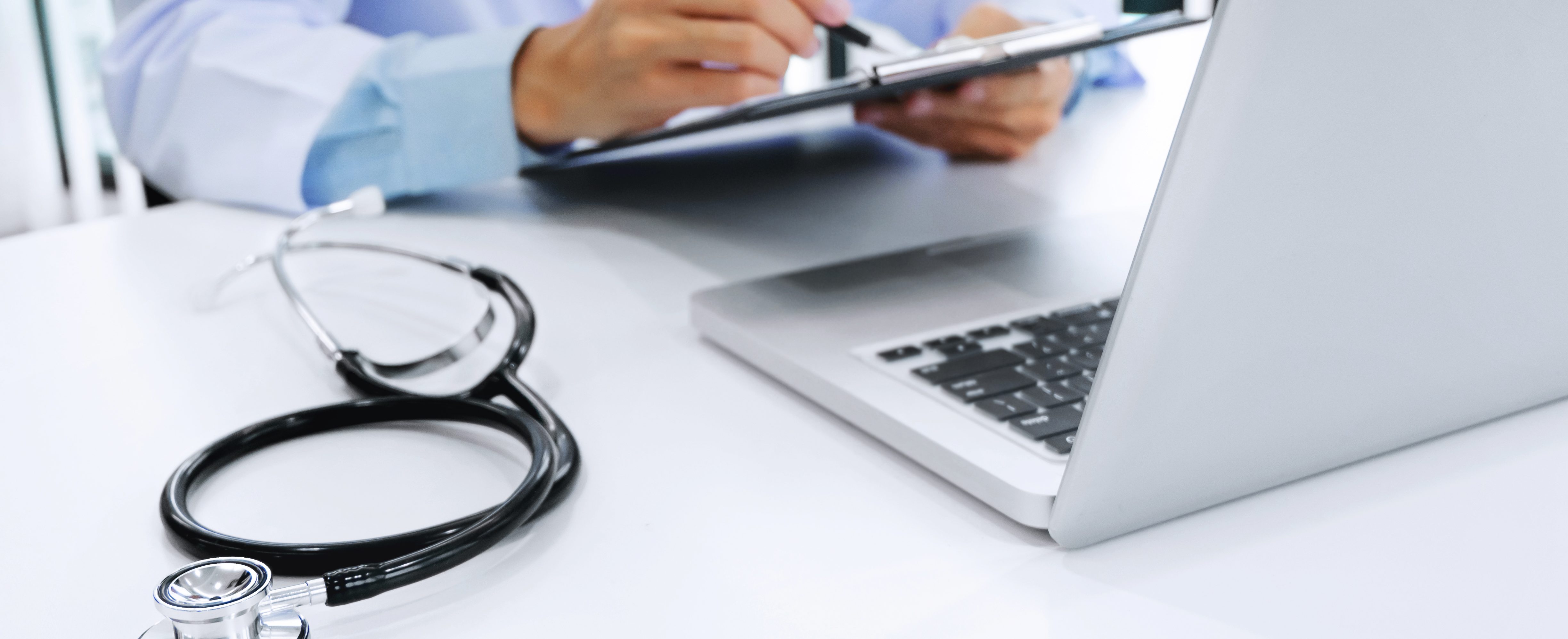 doctor working on laptop with stethoscope and paper clipboard