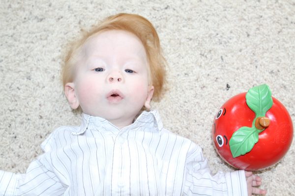 Gauge Neimeier_baby laying on his back next to an vintage apple toy