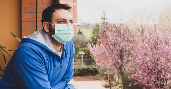 man standing on balcony outside wearing mask